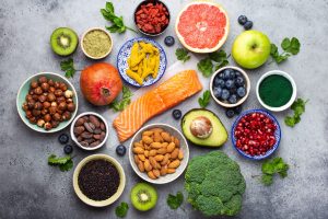 Selection of healthy products and superfoods: salmon, fruit, vegetables, berries, goji, spirulina, matcha, quinoa, chia seeds, nuts. Clean eating concept, gray background, top view, close up